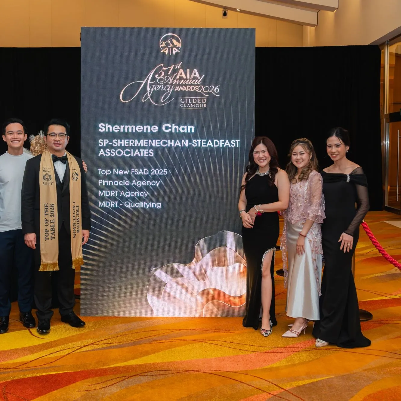 A group standing in front of the screen for the 51st AIA Annual Agency Awards 2026, which lists the name Shermene Chan and award titles