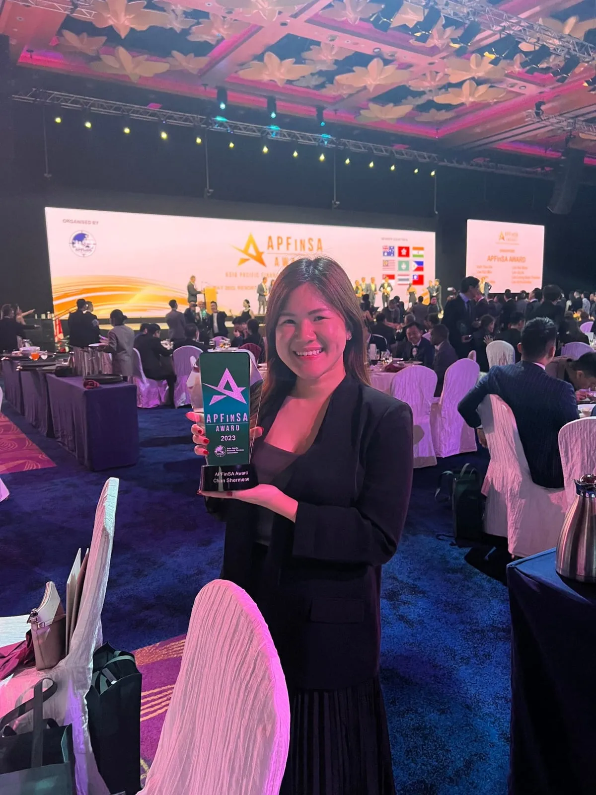 Shermene holding the APFinSA Award 2023 trophy at a large awards dinner
