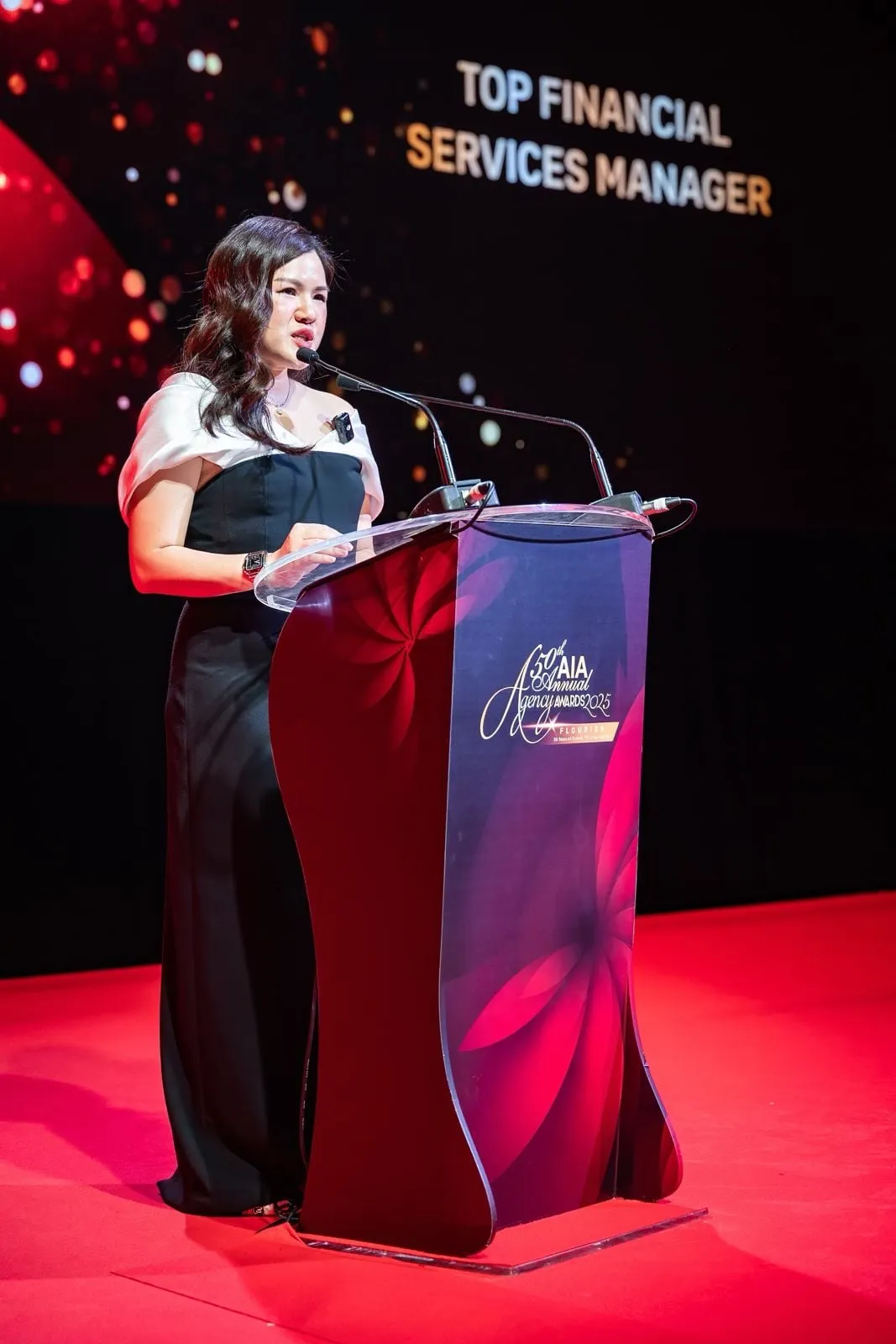 Shermene speaking at a podium at an awards night, with the words Top Financial Services Manager on the screen behind her